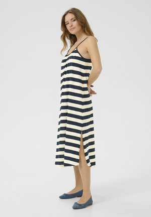 Abito midi a righe in blu navy e crema, caratterizzato da spalline regolabili e spacchi laterali. Abbinato a scarpe basse blu, che mostrano un'estetica casual.