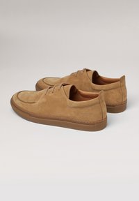 Zapatos de ante con cordones en marrón claro, con puntera redondeada, que cuentan con una suela de goma y detalles cosidos a lo largo del borde.