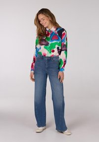 Kleurrijk overhemd met een patroon van blauw, groen, roze en wit. Gecombineerd met hoge blauwe spijkerbroek en witte sneakers.
