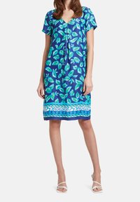 Vestido de manga corta en tela azul con patrones de hojas verdes, escote en V y un dobladillo decorativo con diseños alternos en azul y blanco.