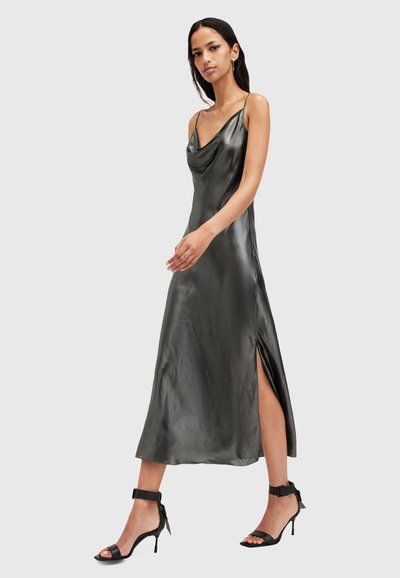 Robe nuisette en satin gris avec un décolleté en cowl, des fines bretelles et une fente sur le côté. Associée à des sandales à talons hauts noires avec des lanières.