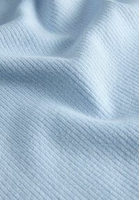 Ανοιχτό μπλε πλεκτό ύφασμα με λεπτή ριμπ δομή και απαλά πτυχώσεις που δημιουργούν απαλές σκιές στην επιφάνεια.