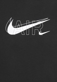 Černá látka obsahuje výrazný bílý text "AIR" s stylizovanou grafikou Nike swoosh integrovanou do designu.