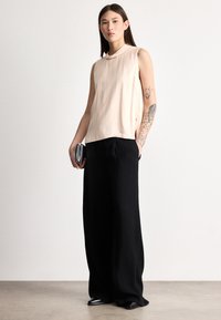 Svetloružový tielkový top s vysokým golierom, skombinovaný s čiernymi širokými nohavicami. Modelka drží striebornú listovú kabelku; na ruke viditeľné tetovania.