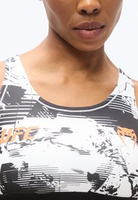 Fekete-fehér sportmelltartó grafikával, narancssárga UFC logóval. Kerek nyakkivágással és vastag vállpántokkal rendelkezik.