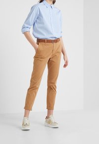 Ljusblå skjorta med uppvikta ärmar, kombinerad med bruna bomullschinos och beige sneakers med gula och röda accenter.