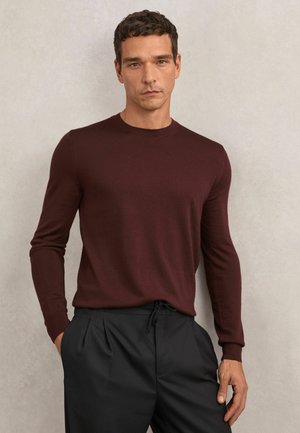 Burgundipunane pika varrukaga kampsun, ümmarguse kaelusega, tekstureeritud kudum, koos mustade plisseeritud pükstega. Fookus istuvusel ilma täiendavate detailideta.