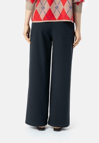 Szerokie, ciemnoniebieskie spodnie z miękkiego materiału o gładkiej teksturze. Czysty, minimalistyczny design z prostym dołem i bez widocznych ozdób.