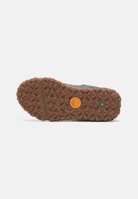 Gray shoe sole with a textured rubber surface, featuring a brown tread pattern, an orange logo, and a green accent detail.