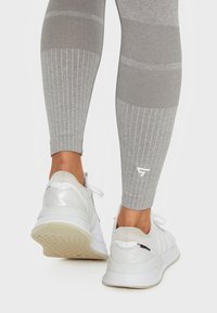 Hellgraue Sportleggings mit geripptem Muster und kontrastierenden horizontalen Streifen, kombiniert mit weißen Sneakers mit strukturiertem Profil.