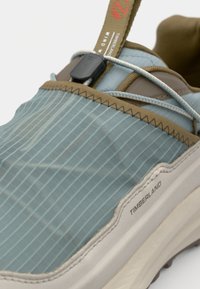 Light blue athletic shoe with a textured upper featuring vertical stripes, elastic laces, and a white sole. Brand logo is visible on the side.