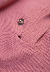Tissu de pull en tricot rose avec des côtes texturées et un petit logo métallique en accent. Le tissu présente une apparence douce, confortable et légère.