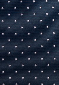 Marinblått tyg med ett strukturerat mönster av jämnt fördelade, små vita prickar, med en räfflad yta och subtil lyster.