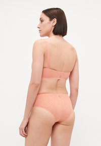 Completo di lingerie color pesca realizzato in tessuto testurizzato. Il reggiseno presenta sottili spalline; le mutandine hanno bordi scallop e una cintura liscia.