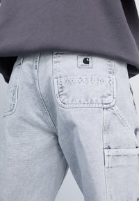 Lichtgrijze cargobroek van denim, met opvallende achterzakken en een label met een zwart logo op de tailleband.