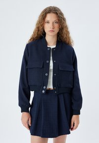 Marineblaue, kurze Bomberjacke mit zwei Vorderaschen, gerippten Bündchen und strukturiertem Stoff, kombiniert mit einem passenden Plisseerock.