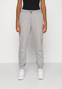 Grå träningsbyxor med dragsko i midjan, sidofickor och ribbade muddar. Har en liten vit textlogotyp på låret. Matchas med vita sneakers.