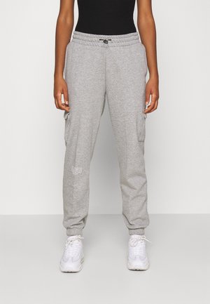 Grijze sweatpants met een trekkoord in de taille, zijzakken en geribbelde boorden. Bevat een klein wit tekstlogo op de dij. Gecombineerd met witte sneakers.