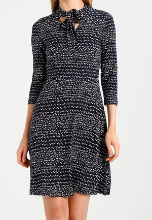 Robe bleu marine avec motif abstrait blanc, manches trois-quarts, taille ajustée et détail nœud à nouer au col.