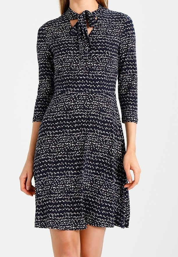 Robe bleu marine avec motif abstrait blanc, manches trois-quarts, taille ajustée et détail nœud à nouer au col.