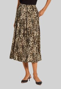 Vrouw in een geplooide midi-jurk met luipaardprint en zwarte slingback hakken met bloemenversieringen.