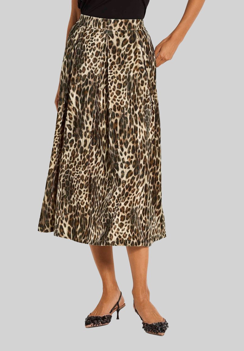 Vrouw in een geplooide midi-jurk met luipaardprint en zwarte slingback hakken met bloemenversieringen.