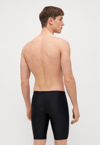 Μαύρα μαγιό κολύμβησης με μήκος μέχρι το μέσο του μηρού, λεία υφή και εφαρμοστό σχέδιο. Χωρίς ορατά σχέδια ή επιπλέον εξαρτήματα.