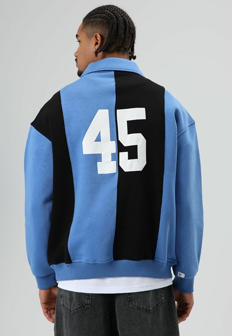 Sweatshirt multicolore comprenant des panneaux bleus et noirs, coupe oversize, avec un grand "45" blanc dans le dos, fabriqué en tissu doux.