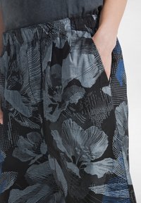 Zwiewna czarna spódnica z niebiesko-szarymi wzorami kwiatowymi, elastycznym pasem, bocznymi kieszeniami i lekką fakturą.