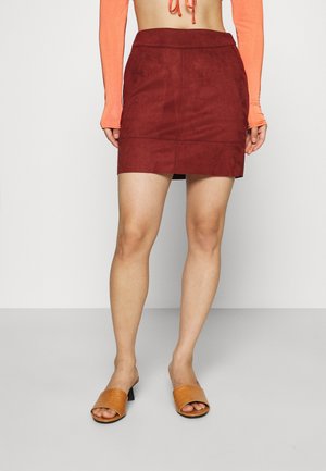 Mini-jupe en daim bordeaux avec une taille ajustée et une fente sur le côté. Associée à des sandales à talons beiges avec un design texturé.