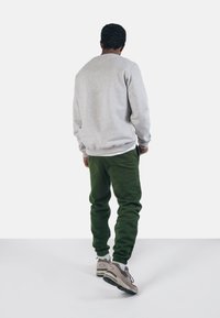 Felpa grigia in cotone, pantaloni jogger verdi con polsini elasticizzati e sneakers beige. Design semplice, vestibilità rilassata, senza loghi o motivi visibili.