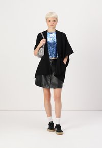 Svart oversize stickad sjal, blå paljetterad crop top, svart läderskirt med knappar, vita strumpor och svarta sneakers. Silverhandväska ingår.