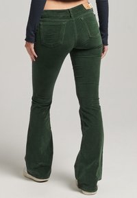Pantalons évasés en velours côtelé vert avec des poches plaquées et une taille ajustée. La texture est côtelée avec une finition douce.