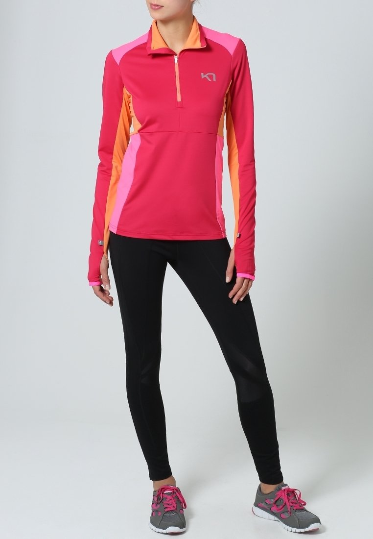 Różowo-pomarańczowa sportowa bluza z długim rękawem i suwakiem do ćwiartki, zestawiona z czarnymi legginsami i szarymi butami sportowymi z różowymi akcentami.