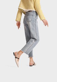 Jeans in denim azzurro chiaro con orlo sfilacciato, abbinati a scarpe slingback beige con cinturino nero e punta affusolata. Giacca gialla a trama.