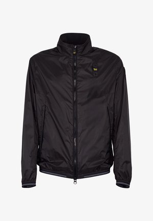 Giacca leggera nera con zip, collo alto, polsini elastici, tasche laterali e piccolo logo giallo sul petto.