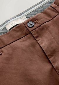 Braune Slim-Fit-Hosen aus glattem Stoff. Mit Knopfverschluss und genähten Nähten. Etikett sichtbar im Bund.
