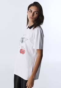 White cotton t-shirt with black collar, featuring a graphic design in gray and red. Loose fit, short sleeves, and round neckline.