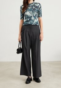 Tight, stickad topp med ett blått och grönt abstrakt mönster, tillsammans med hög midja svarta vida byxor och svarta slip-on skor.