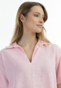 Lys rosa linned blouse med krave, V-hals og korte ærmer. Stoffet har en blød tekstur og en subtil, naturlig finish.