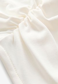Tela blanca suave con detalle elástico fruncido y bordes cosidos, mostrando textura y pliegues.