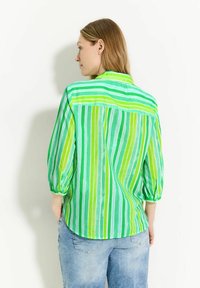 Camisa a rayas verdes con cuello, mangas tres cuartos y un corte holgado. La tela parece semitranslúcida y tiene una textura suave.