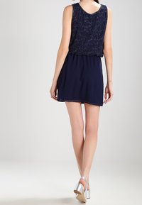 Marinblå klänning med ärmlös design, texturerad överdel och slät kjol. Har en V-halsringning och silverfärgade klackskor.