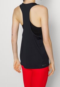 Černý sportovní bezrukávový top s otevřeným zadním dílem, vyrobený z lehkého materiálu. Má zakulacený spodní lem a malé logo v pravém dolním rohu.