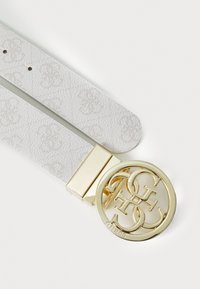 Ceinture blanche texturée avec une boucle circulaire en or présentant des lettres entrelacées "G" et "S". Détail en métal lisse.