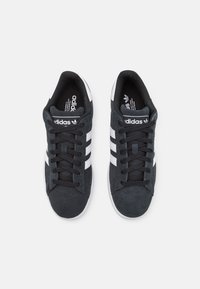 Black suede sneakers with white stripes, round toe, flat laces, and a soft interior lining. Features logo on the tongue and side.