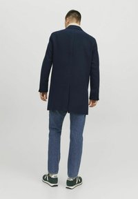 Marinblå kappa i ullblandning med långa ärmar, enkel vent, och klassisk krage, i kombination med ljusa denimjeans och mörka sneakers.