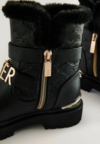 Čierne ankle boots z umelej kože s huňatým čiernym kožúškom na golieri, zlatými zipsami a logom na strane. Textúrovaný vzor na materiáli.