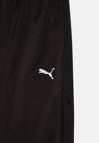 Calções de desporto pretos feitos de um tecido leve, com botões de pressão laterais, apresentando um logótipo branco da Puma bordado no lado esquerdo.