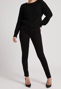 Pull noir côtelé à manches longues, associé à un jean skinny noir et des talons pointus noirs. Tissu lisse et coupe ajustée sur l'ensemble.